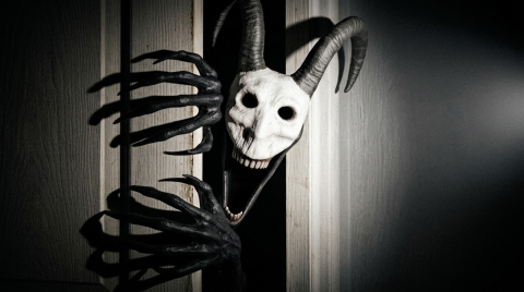 Official promotional art: a horned creature with a pale skull-like face peers around a wooden doorway.